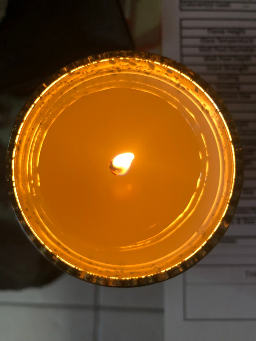 A burning candle seen from above, with a burn test log sheet underneath.