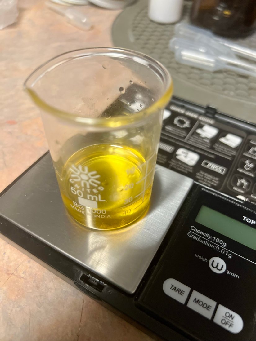 A small glass beaker of fragrance oil on a digital scale.