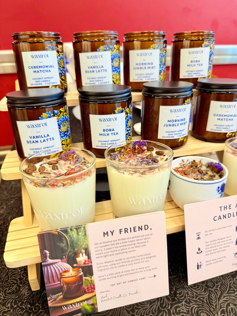 Amber candle jars labelled Ceremonial Matcha, Vanilla Bean Latte, Morning Jungle Mist and Boba Milk Tea on a market booth stand, with two dessert-topped candles and a care card.